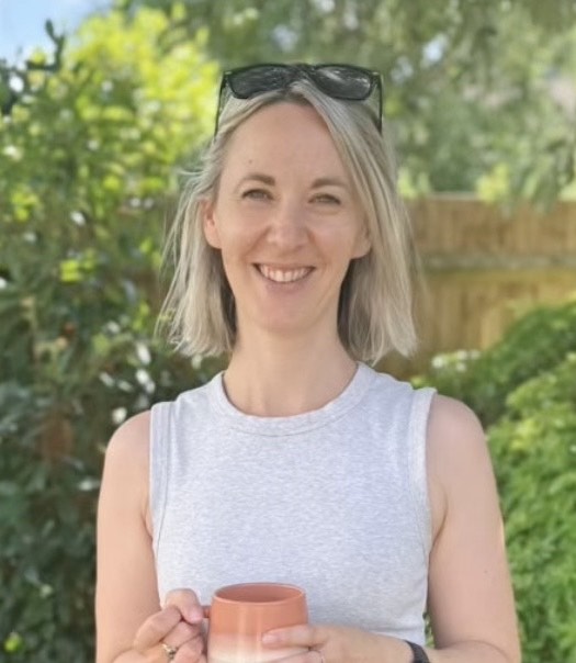 Tessa Spring smiling calmly in her garden and holding a cup of tea